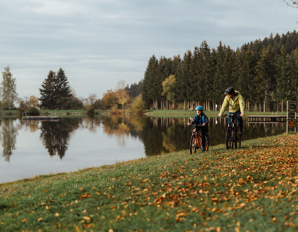 Herbstliches Radfahren_S'INNVIERTEL Tourismus_Matthias Klugsberger Vater und Sohn fahren mit Rad an Badesee-Ufer; herbstliche Stimmung;